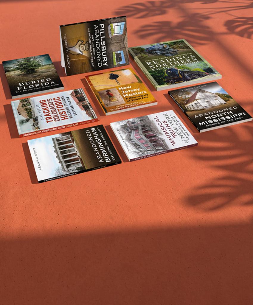 A set of nine books about American history and architecture arranged on a terracotta-colored surface with leaf shadows cast across them.